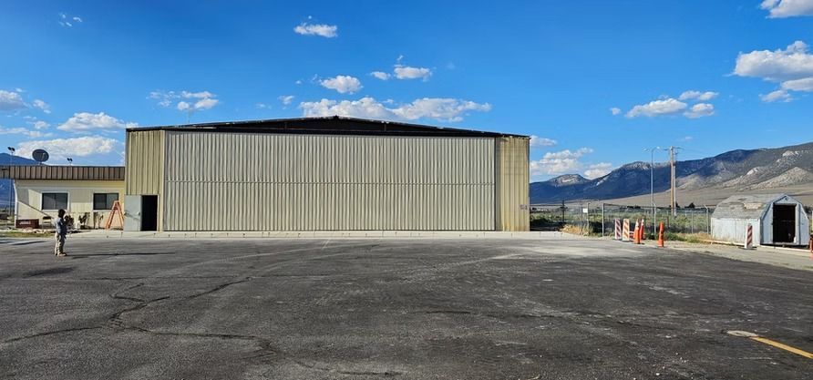 Large hangar on an airfield under a blue sky. Mountains in the distance.