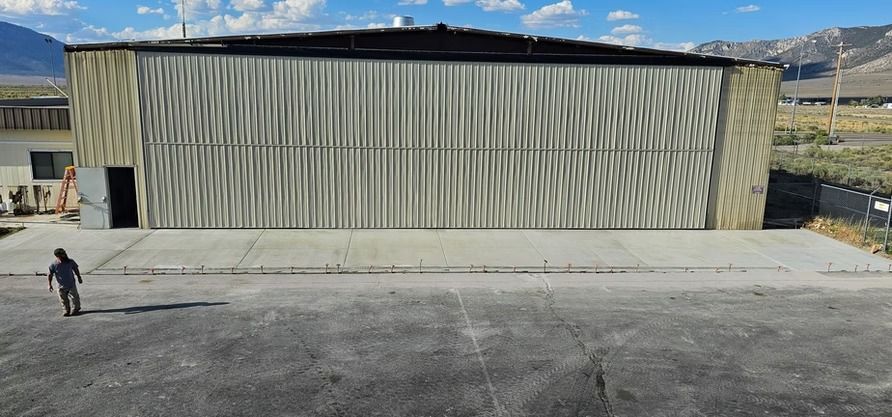 A child walks on the asphalt towards a large industrial building with a corrugated metal facade.