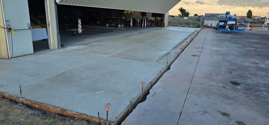 A freshly poured concrete surface extending from an open hangar entrance.