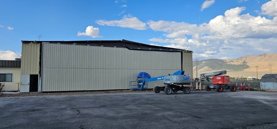 Exterior of a building with damaged roof. Construction equipment is parked in front. Blue sky.