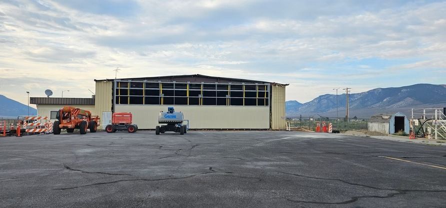 A building with broken windows sits on a cracked asphalt lot, with mountains in the background under a cloudy sky.
