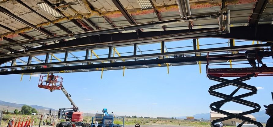 Construction workers on scissor lifts repairing a dilapidated hangar roof. Blue sky, open field.