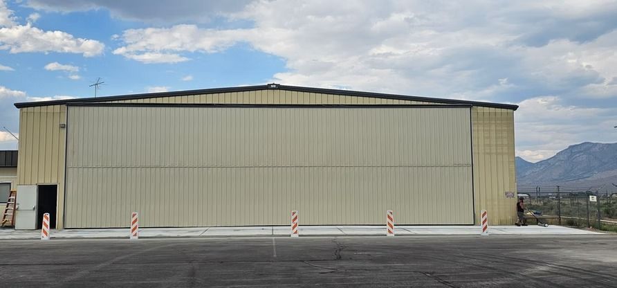 Large hangar with a closed sliding door, set against a cloudy sky. A person walks near the right side.