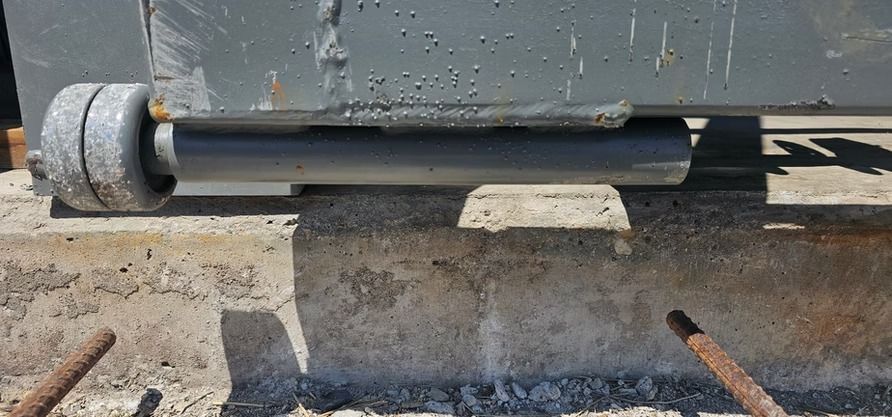A gray roller wheel on a concrete surface, supporting a metal structure.