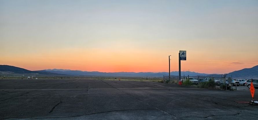 A sunset over a flat landscape with a sign and cars, possibly a parking area.