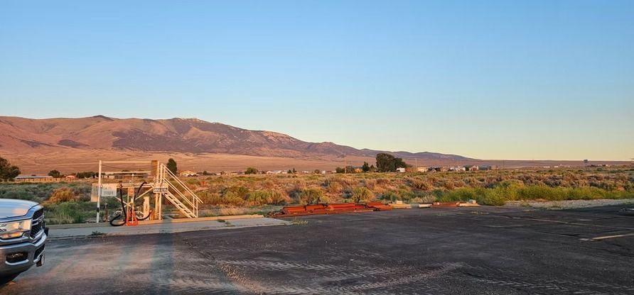 A desert landscape with a wooden structure, vehicle, and mountains under a blue sky.