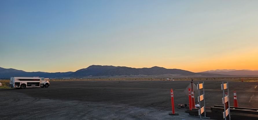 A bus sits on a tarmac at sunset with mountains in the distance.