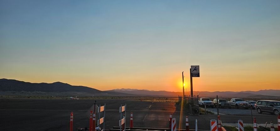 Sunset over a mountainous landscape with a sign and cars in the foreground.