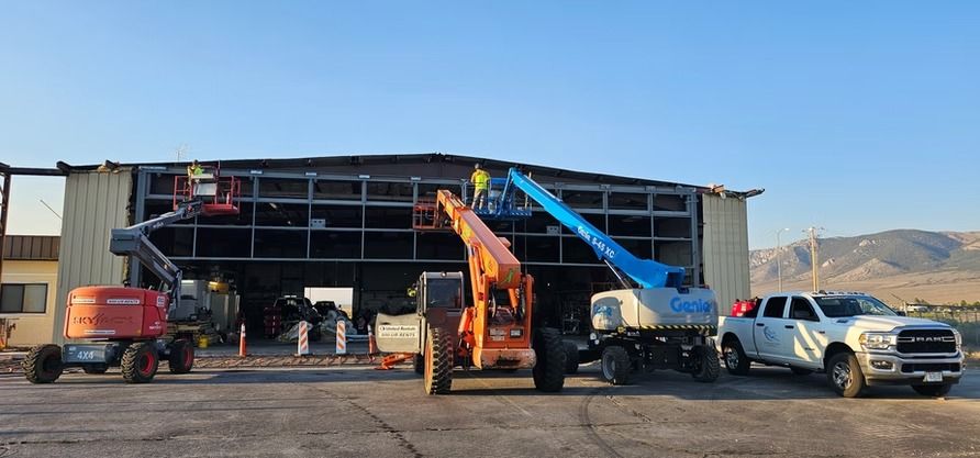 Construction workers use lifts to repair a building's facade. Various construction vehicles are on site.