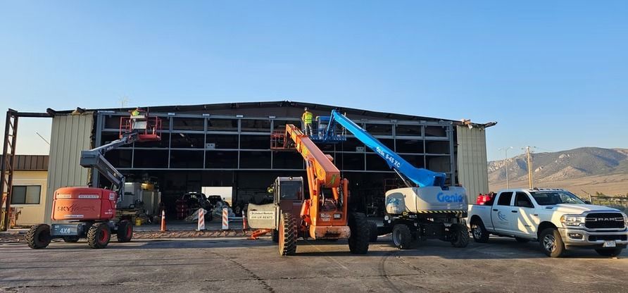 Construction workers use lifts to work on the exterior of a building.  Heavy machinery is parked in front of the building.