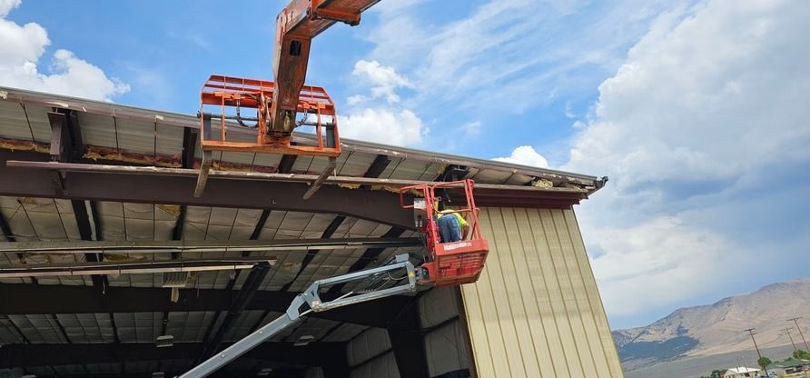 Two orange aerial lifts used for roof repair. Blue sky and mountains in the background.