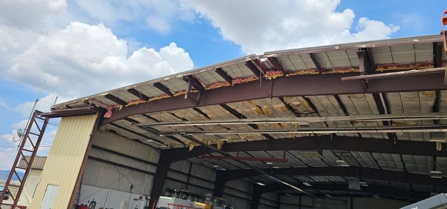 Damaged metal building roof with exposed beams and sky.