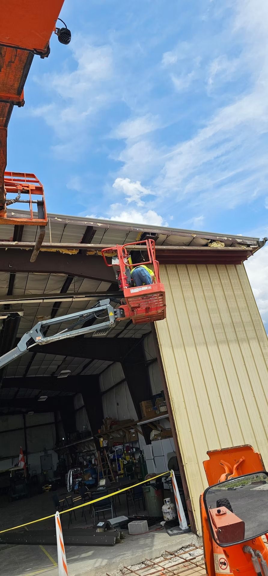 Person in a lift working on a building's roof. Blue sky with clouds.