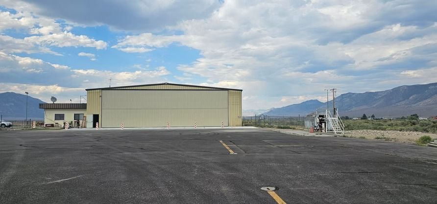 Airport hangar with a paved runway and mountains in the background. Blue sky with clouds.