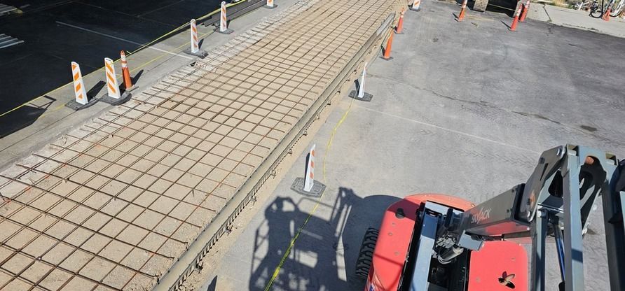 Construction site with a red machine. A concrete section is blocked off by traffic cones.