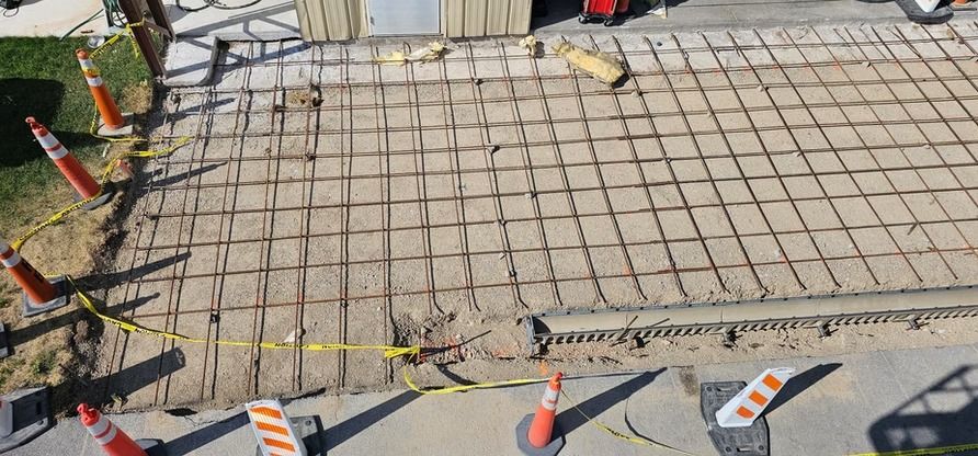 Construction site with metal grid laid out on dirt, safety cones, and caution tape.