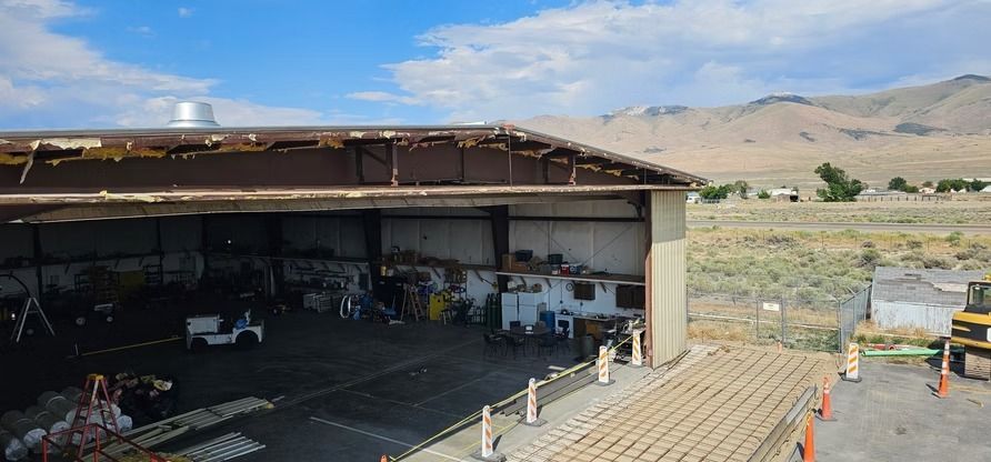 A partially open airplane hangar with mountains in the background, a small white vehicle inside.