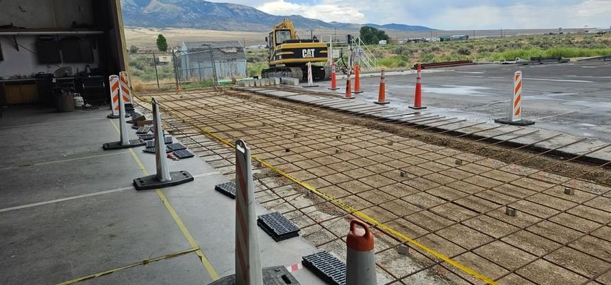 Construction site with rebar grid laid for concrete. Safety cones and barrier posts are visible.