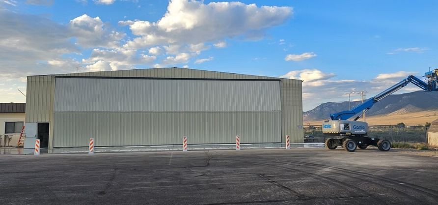 A large hangar with a blue lift in front of it under a partly cloudy sky.