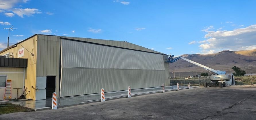 A large building with a long, retractable arm extended. Mountains in the distance under a blue sky.
