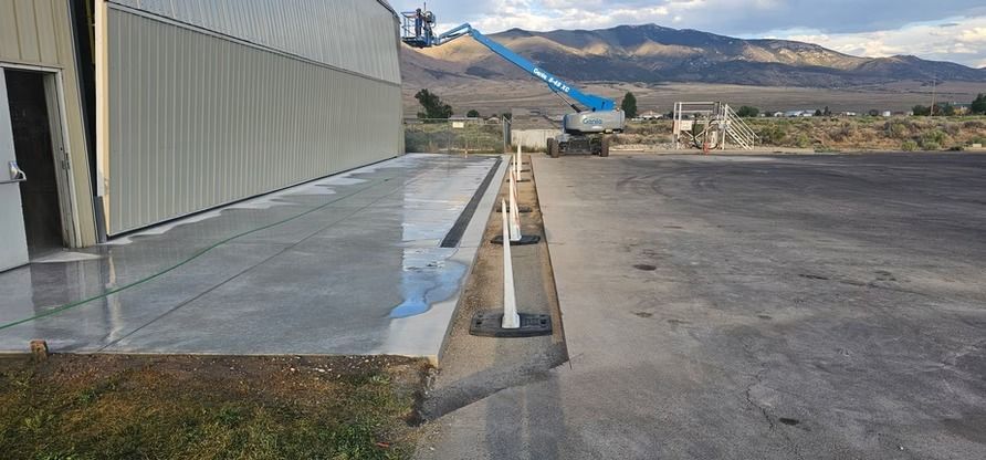 A large industrial building with a concrete apron, a lift, and mountains in the distance.