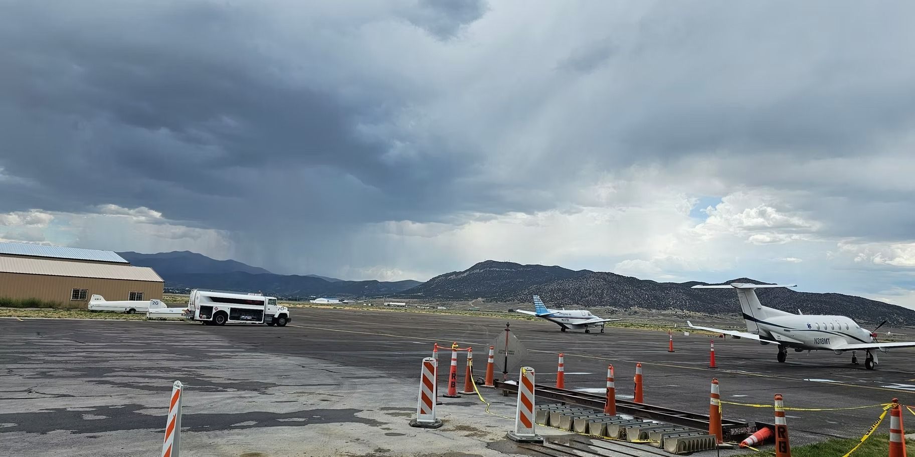 Airport tarmac with two airplanes, a white vehicle, and stormy sky.