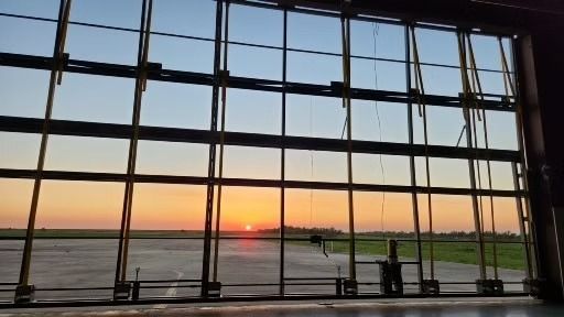 Sunset viewed through an open hangar door, illuminating the sky with orange and yellow hues.