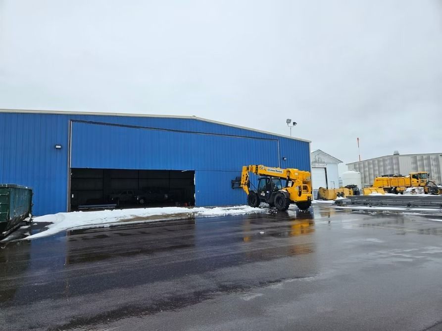 Blue building with open door; yellow forklift outside on wet pavement. Snow on the ground.