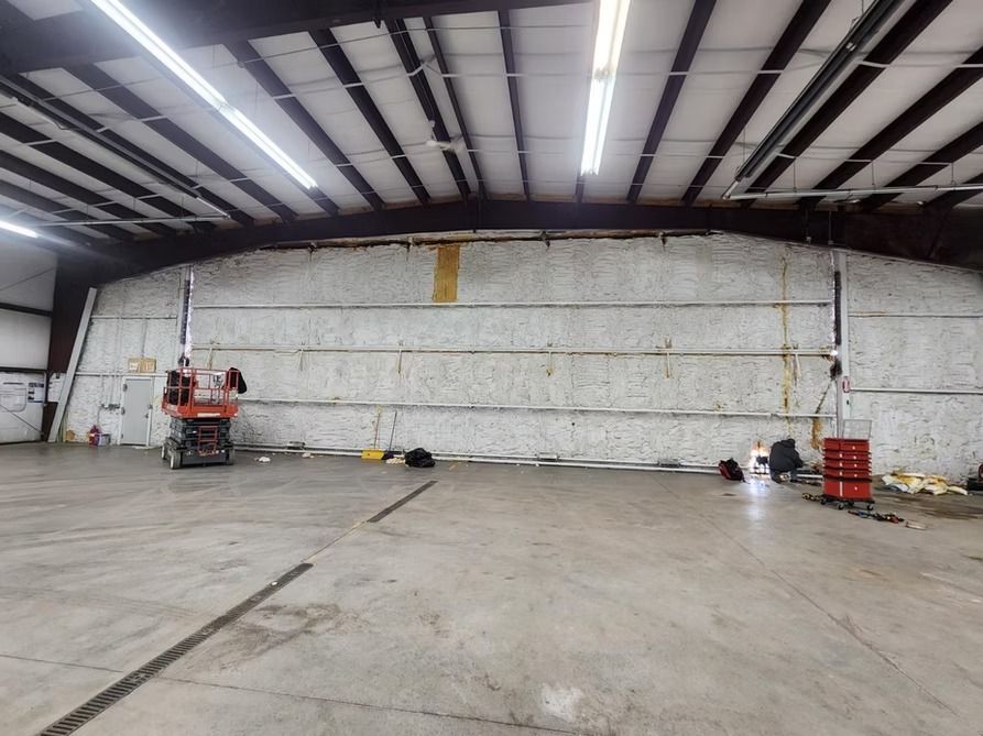Interior view of a large warehouse with exposed insulation on the wall, construction underway.
