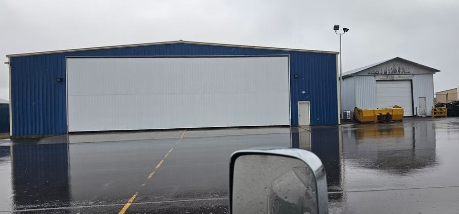 Blue hangar with large white door, next to a smaller white building, on a wet surface.