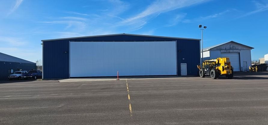 Blue hangar with white door, parked vehicles, sunny day.