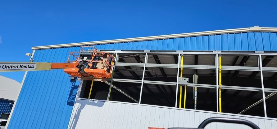 Workers in an orange lift platform repairing blue metal siding on a building, against a clear sky.