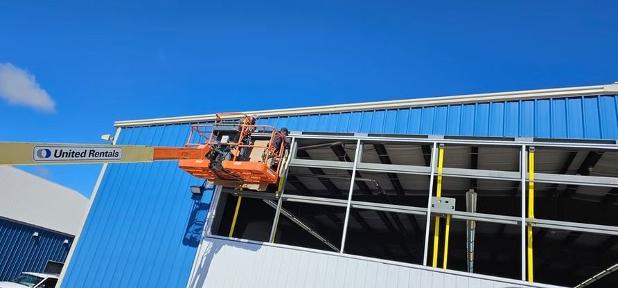 Workers in an orange lift installing panels on a blue building. Clear blue sky.
