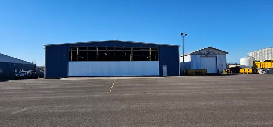 A blue hangar with a large door stands in front of a blue sky.  Small white building on the right.