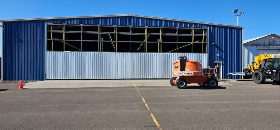 Blue metal hangar with a large open door, orange lift in front.