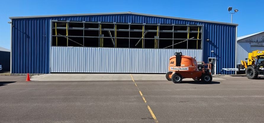 Blue and white metal hangar on a tarmac with orange lift vehicle. Clear blue sky.