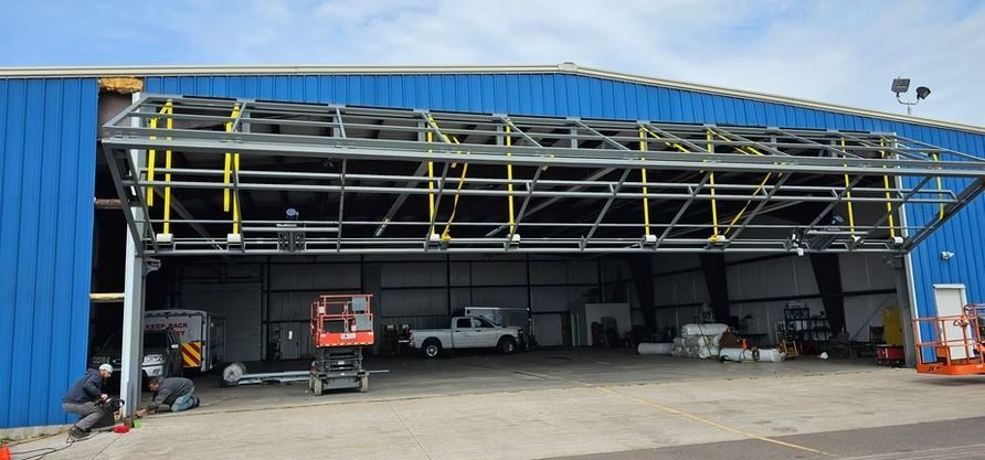 Exterior view of a blue hangar with a large open door, workers and equipment inside.