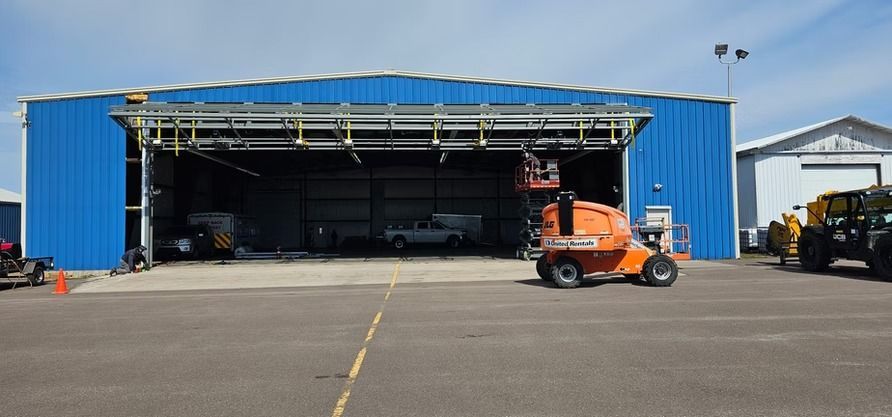 An orange lift in front of a blue hangar with its door open. The sky is blue.