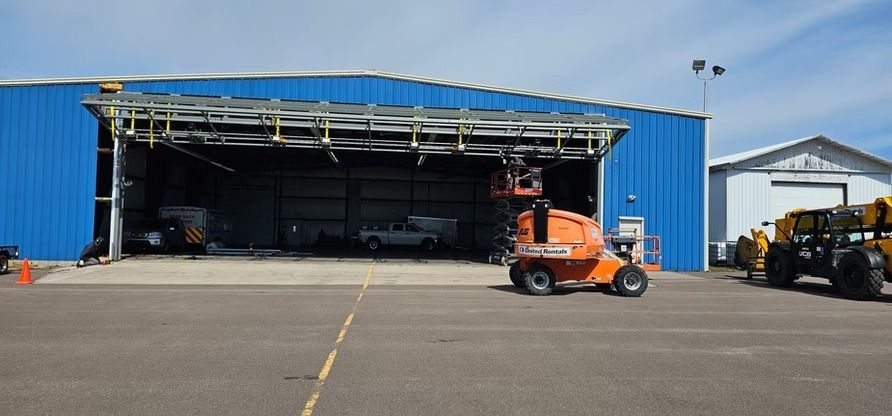 An orange lift is working on the entrance of a blue hangar at an airport.