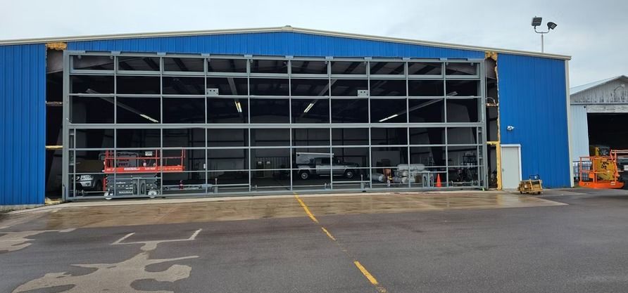 Blue building with large glass door open, showing equipment inside. Wet asphalt in front.