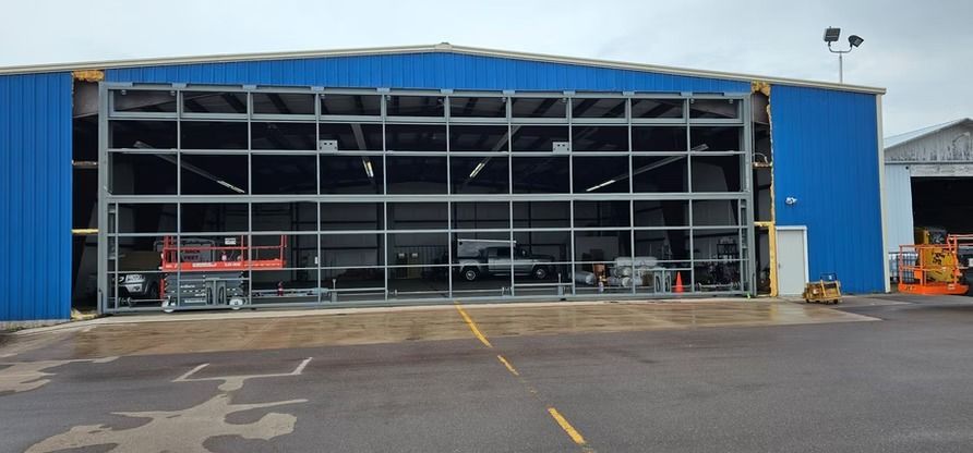 Blue hangar with open glass doors, revealing equipment inside. Yellow parking lines in front.