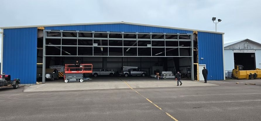 Blue hangar with open door, vehicles inside, people walking in front.