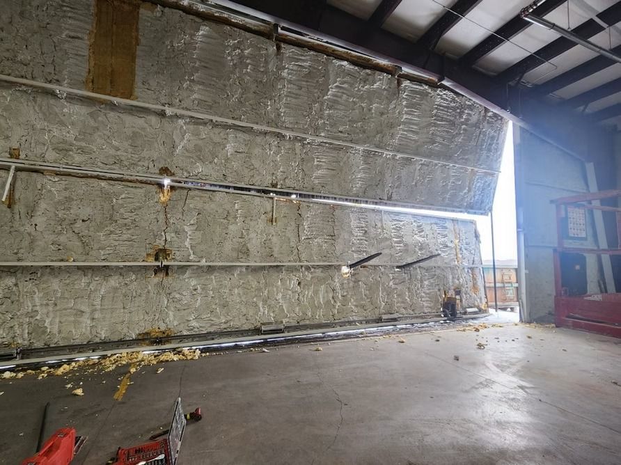 Interior of a building with a large partially open insulated door. Sunlight streams through the opening.