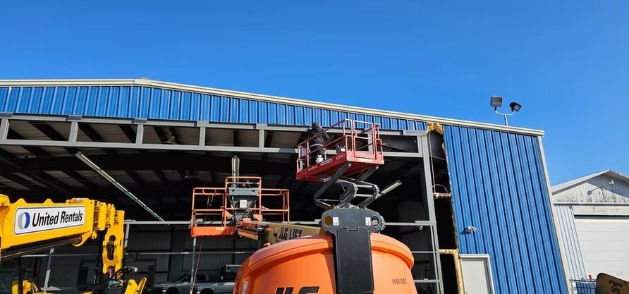 Construction workers using lift equipment to work on a blue metal building under a clear sky.
