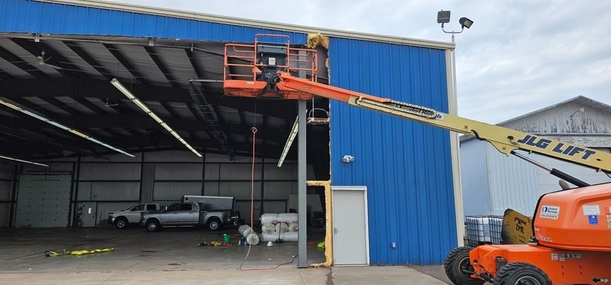 A lift is used on a blue building. A worker is in the lift. The building has a white door.