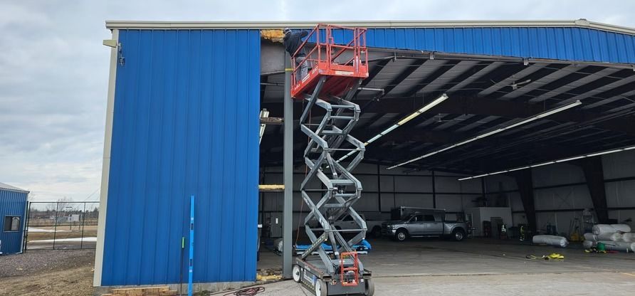 A scissor lift near a blue metal building with an open door; a worker is in the lift.