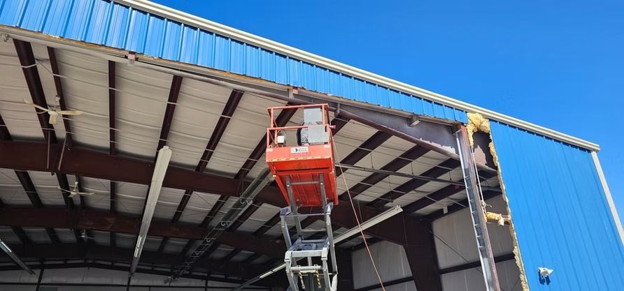 A person in a lift working on a blue and white building under a clear sky.