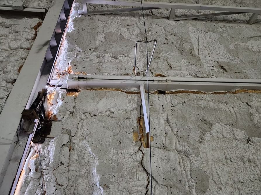 Close-up of a damaged concrete wall with cracks and metal framing. Brown rust is visible.