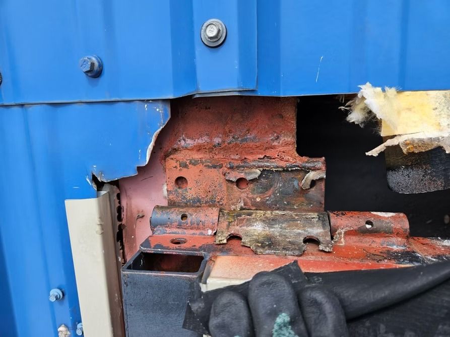 Damaged blue metal wall exposing rusty support brackets and insulation.