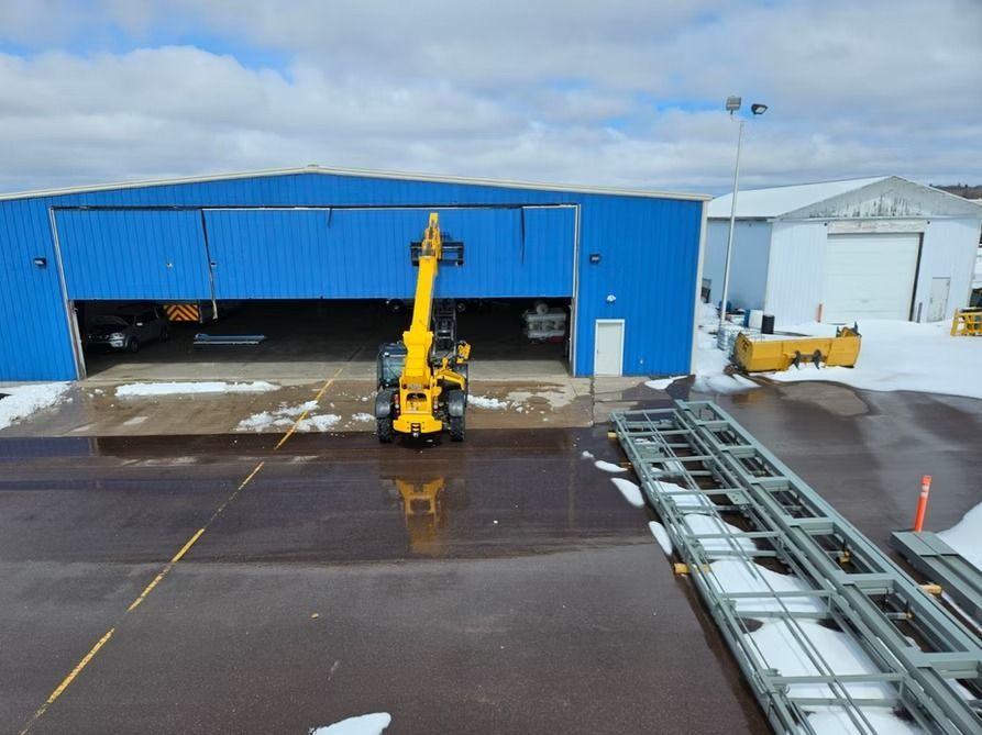 Yellow forklift in front of a blue hangar with snow on the ground, and a white building in the background.